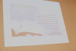 Slajd prezentacji z cytatem motywacyjnym na tle częściowo otwartej książki. Tło ma jasny, ciepły, brzoskwiniowy odcień. Centralna treść slajdu to cytat w języku polskim: „Każdy ma swoje Kilimandżaro. Dla jednego będzie to szczyt górski, dla innego podjęcie pracy czy jej zmiana, dla jeszcze kogoś innego samodzielne przejście do łazienki. Każdy ma coś do zdobycia. Każdy ma swój szczyt!". Poniżej widnieje podpis: „Angelika Chrapkiewicz-Gądek, Zdobądź swój szczyt. Uwierz w swoją siłę"