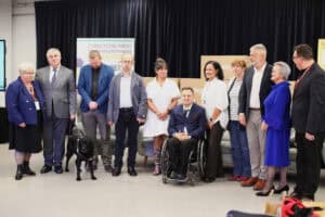 Grupa jedenastu osób, w strojach formalnych pozuje do zdjęcia na scenie. W centrum kadru mężczyzna na wózku (Robert Jagodziński). Obok niego stoi kobieta w białej sukience. Z lewej strony stoi mężczyzna (Paweł Wdówik), a przy nim czarny pies przewodnik. W tle widoczny jest baner Stowarzyszenia Pomocy Dzieciom Niepełnosprawnym „Krok za Krokiem" i stos tekturowych pudeł