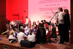 Scena, na której wokół wykonawców siedzi na podłodze grupa dzieci i młodzieży. Po prawej stronie młoda kobieta ze skrzypcami śpiewa do mikrofonu, a obok niej stoi inna kobieta. W tle, na ekranie oświetlonym na biało-czerwono, wyświetlany jest tekst piosenki (patriotycznej, z tekstem "Oj, da, oj da dana..." oraz fragmentem "Gdy Moskal, psia wiara..."). Po lewej stronie widać muzyków grających na gitarze i keyboardzie. Dzieci są ubrane w stroje galowe lub ludowe