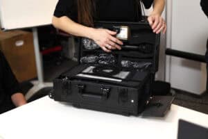 Bliskie ujęcie dłoni kobiety sięgającej po mikrofon ukryty w specjalnej, wyłożonej gąbką pokrywie otwartej czarnej walizki. Walizka zawiera pętlę indukcyjną, prezentowaną uczestnikom szkolenia