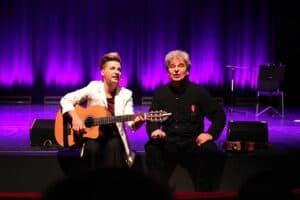 Dwoje artystów (Karolina Czajka i Michał Stanowski) siedzi na brzegu sceny, dają występ muzyczny. Kobieta z krótkimi, jasnymi włosami w białej marynarce gra na gitarze akustycznej. Obok niej siedzi mężczyzna w czarnym stroju, z odznaczeniem przypiętym do koszuli. Tło stanowi fioletowa kurtyna