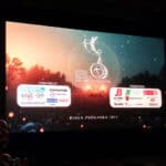 Ekran kinowy wyświetla planszę sponsorską XII Festiwalu Filmowego Twórczości Osób Niepełnosprawnych w Białej Podlaskiej 2025; plansza ma ciemne tło, jest to wieczorny pejzaż, na którym widnieje statuetka festiwalu oraz logotypy patronów medialnych i partnerów festiwalu