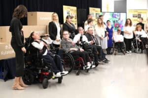 Szerokie ujęcie grupy osób prezentującej się na scenie. Na pierwszym planie po lewej stoi kobieta w ciemnej sukience, patrzy na grupę. Obok niej siedzą cztery osoby na wózkach, a za nimi stoi kilka kolejnych osób. W tle po lewej widoczny jest stos tekturowych pudeł z napisami „Konwencja", „Pedagogika" i „dr Zofia Kułakowska". Po prawej widoczny jest duży monitor z wyświetloną grafiką i napisem „BOCCIA". Z tyłu ustawiono banery z historią stowarzyszenia