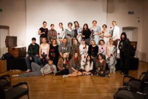 Pamiątkowe zdjęcie grupowe uczestników projektu „Tableau vivant” – młodzieży z Zespołu Szkół nr 2 w Lubartowie. Dwudziestoczteroosobowa grupa pozuje na scenie w trzech rzędach, część w kostiumach scenicznych, część we współczesnych ubraniach, każdy z czerwoną różą w dłoni