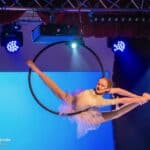 Dziewczynka ubrana w kremowy kostium wykonuje akrobacje na czarnej obręczy, zawieszonej w powietrzu. Fot. Agnieszka Łyko Fotografia