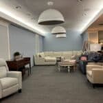 Wnętrze pokoju spotkań, wyposażone w meble wypoczynkowe: sofy, fotele i niski, okrągły stolik. Ściany pomieszczenia są jasnoszare, ozdobione białymi sztukateriami. Przy suficie zamontowano trzy duże białe lampy