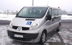 Srebrny van Renault z piktogramem osoby na wózkach inwalidzkich, zaparkowany na zaśnieżonym, utwardzonym terenie w pobliżu budynków mieszkalnych
