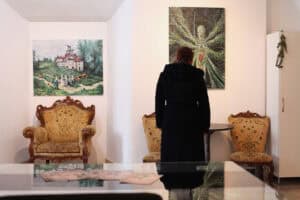 Kobieta ogląda obraz Jana Kaweckiego w salonowej części galerii. Na szklanym stole leżą pocztówki promocyjne.