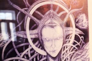 Zbliżenie na fragment fioletowej grafiki Jana Kaweckiego z bladą twarzą postaci i gęstą, organiczną strukturą.