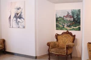 Narożna ekspozycja w galerii. Na ścianie wisi wielkoformatowy, ekspresyjny portret postaci, autorstwa Jana Kaweckiego