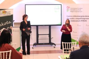 Barbara Sadowska-Burlita i Iwona Podkowa-Nowak) stoją obok ekranu z logo CIDON i PFRON, prowadzą rozmowę lub debatę. Widok z widowni