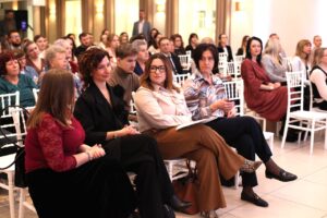 Publiczność konferencji siedzi w rzędach na białych krzesłach w eleganckiej sali. Na pierwszym planie siedzą od lewej: Barbara Sadowska-Burlita, Iwona Nowak-Podkowa, Monika Wac, Irena Kijek.