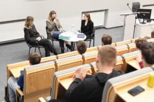 Trzy kobiety biorą udział w dyskusji panelowej przy okrągłym stoliku w auli. Małgorzata Szumowska mówi do mikrofonu. Obok niej siedzą dr hab. Ewelina Podgajna, prof. UMCS, oraz Sylwia Kubica. Widok z widowni