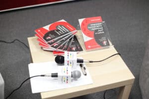 Na małym jasnym stoliku wyeksponowano książki Roberta Litwińskiego: „Integracyjne Centrum Sportu i Rehabilitacji 'Start' w Lublinie. Historia i teraźniejszość (1945-2025)”. Obok nich leżą dwa mikrofony reporterskie z kostkami z logotypami Centrum Historii Sportu w Lublinie.