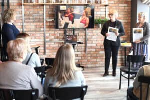 Edyta Filipczak i Marta Rak stoją przed publicznością, trzymając certyfikaty w białych ramkach. Obok nich ekran z prezentacją.