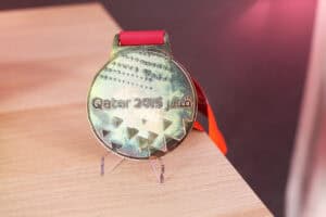 Brązowy medal „Qatar 2015” na przezroczystym stojaku, medal ma czerwoną wstążkę. Powierzchnia medalu ma teksturę z małymi wgłębieniami i trójkątnymi wzorami w dolnej części