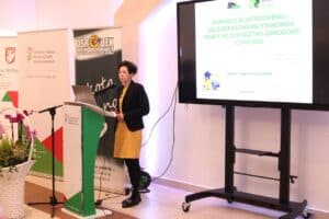 Marzena Słotwińska-Kanar stoi przy mównicy. Prezentuje slajd Miejskiego Urzędu Pracy w Lublinie pt.„WSPARCIE W ZATRUDNIENIU – OD DOFINANSOWANIA STANOWISK PRACY PO DORADZTWO ZAWODOWE I COACHING”.