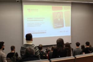 Aula akademicka. Na ekranie wyświetla się slajd z napisem ‘AGORA AKADEMICKA’, tytułem wykładu ‘MIĘDZY KONWENCJĄ A CODZIENNOŚCIĄ’, datą 14/01/2026 i logo UMCS. Widok z widowni.