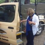 Afryka Południowa. Kobieta stoi obok zaparkowanej furgonetki z otwartymi drzwiami. Na drzwiach widoczny napis „Africa Spear (…) Park Safaris”