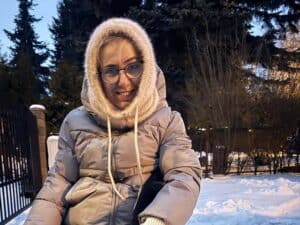 Na zewnątrz w zimowej aurze siedzi uśmiechnięta Aleksandra Górska (autorka artykułu) w okularach, ubrana w beżową zimową kurtkę i włochaty, wełniany kaptur
