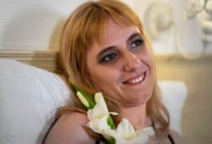 Blondynka z grzywką, uśmiecha się i patrzy w górę. Po lewej stronie na ramieniu ma ułożony kwiat - biały mieczyk; fot. Paweł Pietrzak - Hokus Pokus