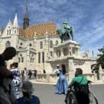 Budapeszt, 2025. Baszta Rybacka i Kościół Macieja. Na słonecznym placu przy pomniku św. Stefana, spacerują turyści. Po prawej mężczyzna na wózku