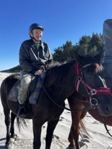 Wrzesień 2025, Jantar. Na piaszczystej plaży mężczyzna w kasku jeździeckim siedzi na koniu o ciemnym umaszczeniu. W tle widać wydmy z roślinnością, a niebo jest bezchmurne i błękitne