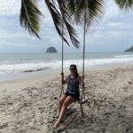 Piaszczysta plaża nad morzem. Na palmie wisi huśtawka, na której siedzi brunetka w okularach przeciwsłonecznych. Niebo jest lekko zachmurzone, na morzu delikatne fale. Wiatr zgina liście palmy i porusza włosy kobiety