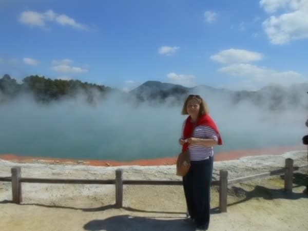 Nowa Zelandia, 2013. Kobieta stoi przed parującym gorącym źródłem. W tle zielone, zalesione wzgórza