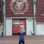 Sebastian Paca przed bramą nr 4 stadionu Widzew Łódź, ubrany granatowo-czarny dres ma uniesione ręce