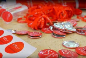 Na blacie leżą materiały promocyjne z logo "Paszport Życia": Przypinki, naklejki i smycze