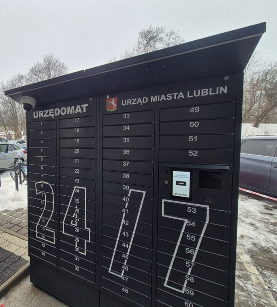 Czarny, samoobsługowy paczkomat z napisami URZĘDOMAT i URZĄD MIASTA LUBLIN, wyposażony w ponumerowane przegródki oraz panel dotykowy.
