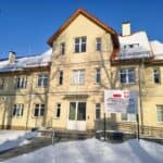 Piętrowy budynek Wspomaganej Społeczności Mieszkaniowej w Bartoszycach w zimowej scenerii, z pokrytym śniegiem otoczeniem i błękitnym niebem w tle