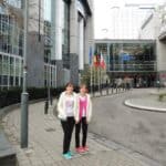 Siostry Wróbel ubrane w czarne spodnie i białe kurtki stoją na tle budynku Parlamentu Europejskiego