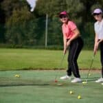 Siostry Wróbel w dresach, T-shirtach i czapkach bejsbolówkach, grają w golfa na polu golfowym