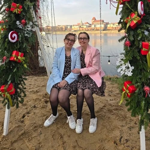 Uśmiechnięte Magdalena i Marta siedzą na huśtawce, nad Wisłą w Toruniu.