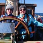 Siostry Wróbel ubrane w czapki i niebieskie kurtki stoją na łódce trzymając w dłoniach ster