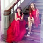 Magdalena i Marta ubrane czerwone balowe suknie siedzą na starych schodach; fot. BoCerba Photography