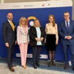 Pięć osób – między dwoma mężczyznami stoją trzy kobiety – pozuje do zdjęcia na tle ścianki z logotypem Centrum Komunikacji dla Osób z Niepełnosprawnościami