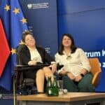 Dwie uczestniczki panelu dyskusyjnego siedzą przy niewielkim stoliku, w tym jedna na wózku elektrycznym. W tle ścianka z logotypami Ministerstwa Funduszy i Polityki Regionalnej