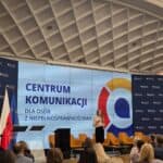 Wystąpienie konferencyjne dr Moniki Zimy-Parjaszewskiej; w tle ekran multimedialny z napisem i logotypem Centrum Komunikacji dla Osób z Niepełnosprawnościami