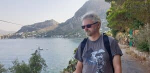 Rafał Charłampowicz ubrany w grafitowy t-shirt ze statkiem kosmicznym stoi na tle jeziora i gór