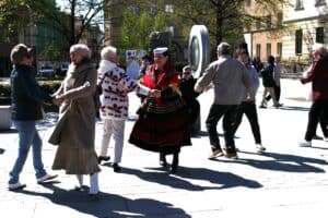 Kilka par tańczy na Placu Litewskim. W centrum kobieta w stroju ludowym trzyma za ręce inną uczestniczkę w białej, wzorzystej kurtce. Po lewej stronie para kobiet w dynamicznym obrocie