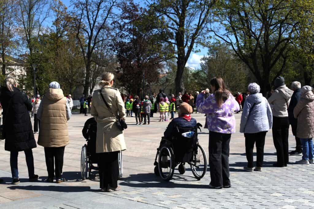 Osoby obserwują wydarzenie na Placu Litewskim; na pierwszym planie osoba na wózku, w tle dzieci w kręgu.