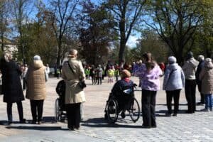 Osoby obserwują wydarzenie na Placu Litewskim; na pierwszym planie osoba na wózku, w tle dzieci w kręgu.