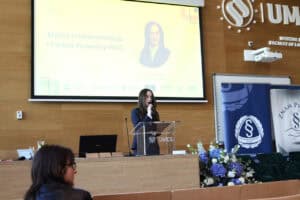 Karolina Flor przy pulpicie prowadzi wykład pt. „Efekty i rekomendacje I Forum Prawnicy-NGO”. Na ekranie za nią widać jej zdjęcie i nazwisko.
