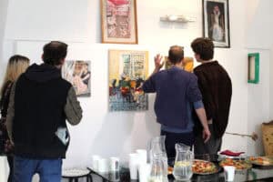 Trzej mężczyźni i kobieta odwróceni przodem do białej ściany galerii, przyglądają się z bliska wyeksponowanym obrazom