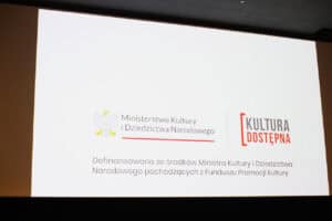Ekran kinowy z logotypami Ministerstwa Kultury i Dziedzictwa Narodowego oraz programu Kultura Dostępna. Poniżej napis: „Dofinansowano ze środków Ministra Kultury i Dziedzictwa Narodowego pochodzących z Funduszu Promocji Kultury”.