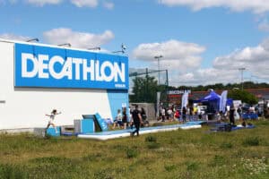 Plenerowe wydarzenie sportowe przed budynkiem Decathlon Węglin. Na trawiastym terenie rozstawiono dmuchane ścieżki akrobatyczne, przeszkody oraz niebieski namiot Fundacji Decathlon, wokół którego gromadzą się ludzie.