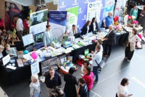 Widok z góry na stoiska informacyjne rozstawione w holu. Widoczny jest długi stół z materiałami promocyjnymi, książkami i ulotkami. Przy stoiskach Pedagogicznej Biblioteki Wojewódzkiej im. KEN w Lublinie rozmawiają ze sobą wystawcy i uczestnicy.
